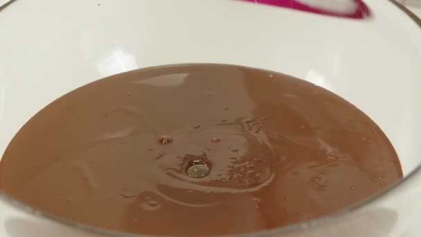Nahaufnahme, bei der Schokoladensplitter in dunkle geschmolzene Schokolade in Glasschüssel gegossen werden — Stockvideo