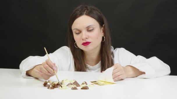 Mooie chef-kok versieren premium chocolade snoepjes met goud folie met behulp van borstel — Stockvideo