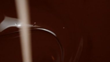 Tahta çubuk, parlak, erimiş siyah çikolatayı anaforlar ve girdaplarla karıştırır.