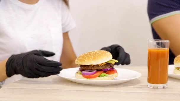 Close up chica joven en guantes de ruber negro toma deliciosa hamburguesa casera, comida rápida — Vídeo de stock