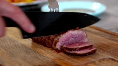 Evdeki adam büyük, sulu, orta boy bifteği siyah bıçakla doğruyor.