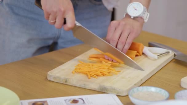 Крупним планом жіночий кухар нарізає свіжу моркву скибочками, готуючи веганську гарнітуру — стокове відео