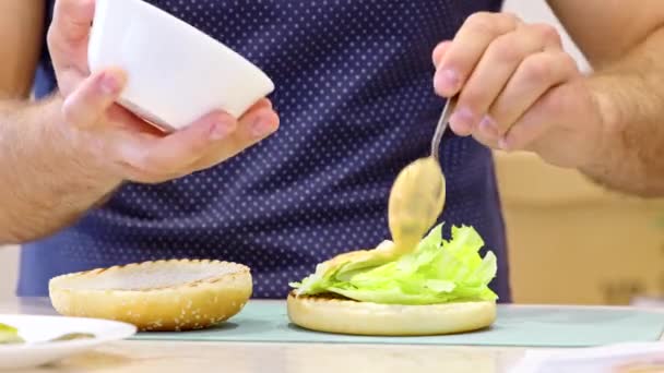 A cozinhar hambúrgueres em casa. chef amador adiciona molho ao pão para fazer hambúrguer — Vídeo de Stock