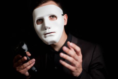 Siyah bir zemin üzerine beyaz maskeli bir adam Close-up. Kollarını kaldırdı silahı tutan