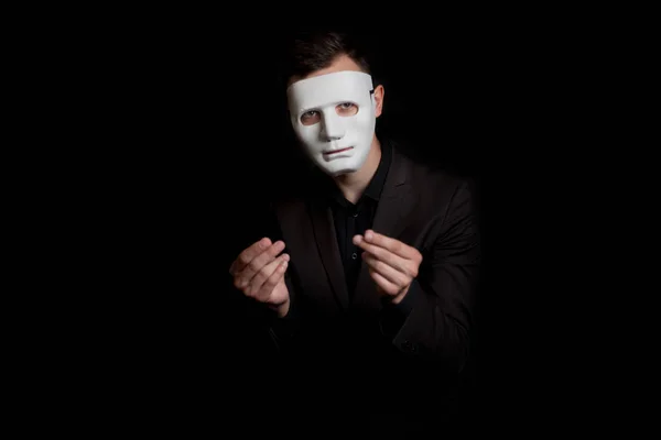 Portrait of a man in a white mask on a black background. Shows a