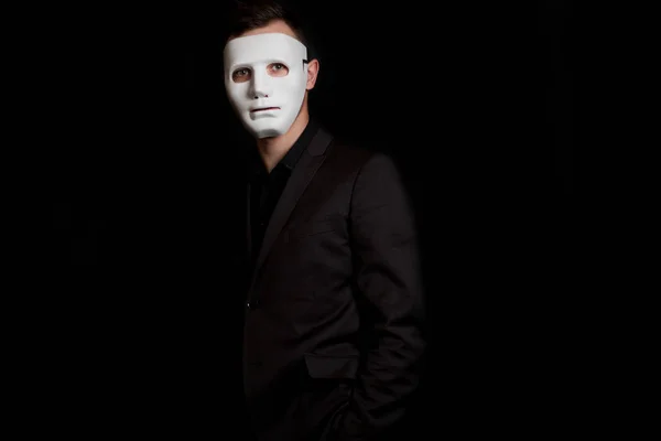 A man stands on a black background in a white mask. Incognito, a