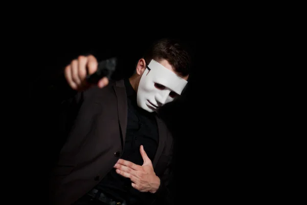 A man in a white mask on a black background, holding a pistol an