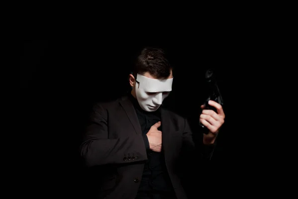 A man in a white mask on a black background, holding a pistol an