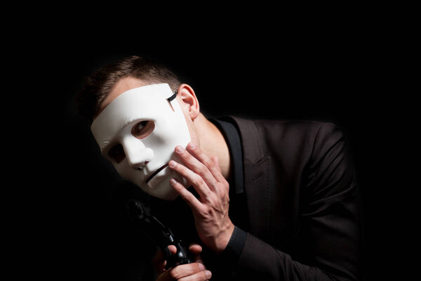 Close-up of a man in a white mask on a black background. Holds t