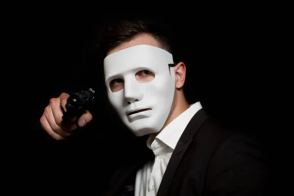A man in a white mask on a black background, threatens with a gu