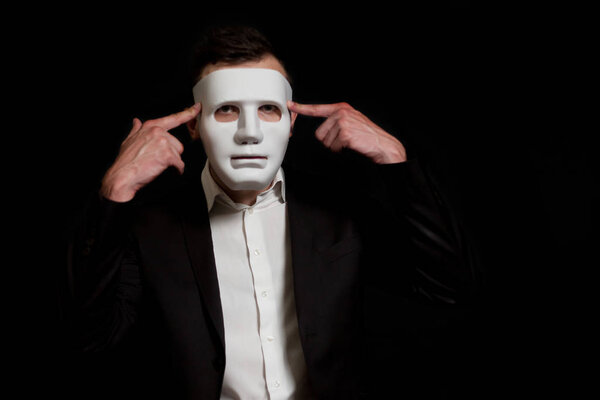Человек в белой маске на черном фоне скручивает пальцы
