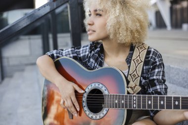 Kıvırcık kız yaratıcılık yapıyor, o sokakta gitar çalıyor.