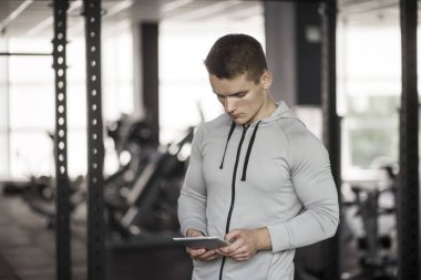 Uygulama ile egzersiz planı kullanan atletik genç adam eğitim spor salonunda, önce dijital tablet. Vücut geliştirme kavramı