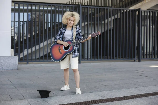 Woman African-American appearance, street musician earns money by playing the guitar