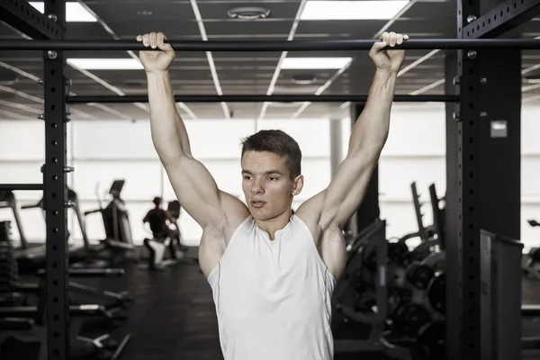 Sporcu kaslı erkek model spor salonunda yatay çubuğa yanaşıyor.