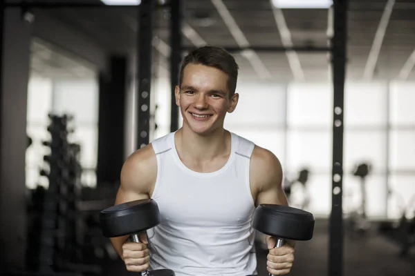 Concentrated young fitness man working out with dumbbells in gym