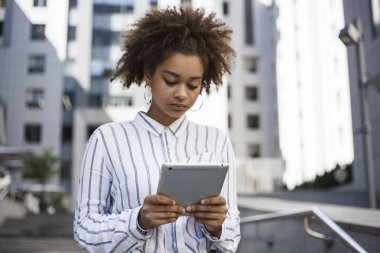 Esmer kız bir tablet onun elinde tutan ve üzerinde çalışıyor. O bir ofis sokakta Binası yakınında Standları