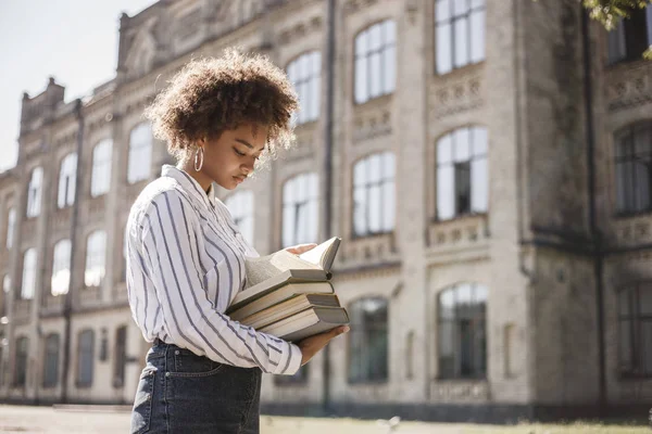 浅黒い肌の少女は 大学近くの路上に立っています 彼女は彼女の手と読み取りの書籍を保持しています — ストック写真