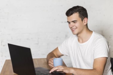 Adam masada oturur ve Kupası elinde tutuyor. Bir dizüstü bilgisayarda çalışır.