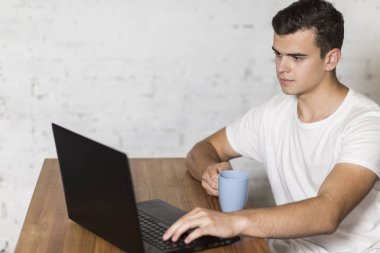 Genç bir adam, masada oturan ve kahve içme dizüstü bilgisayarda çalışıyor.