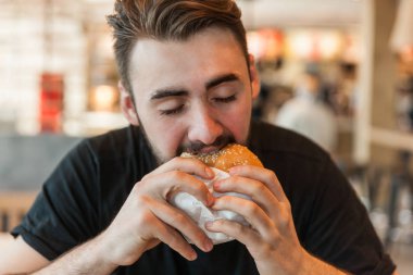 Kafede öğle yemeği. Adam bir hamburger yiyor.