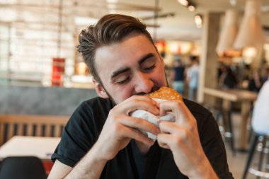 Kafede öğle yemeği. Adam bir hamburger yiyor.