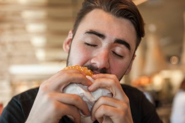 Yakın çekim bir adam bir hamburger elinde tutan ve ısırma