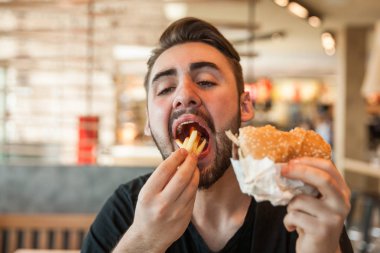 Kafede öğle yemeği. Bir adam kızarmış patates yiyor ve hamburger tutar.