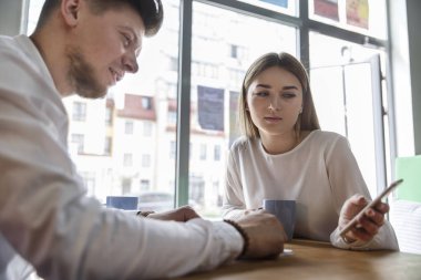Sakallı adam kızla masada oturuyor ve telefon üzerinde görünüyor. O tutan ve gülümseyerek. Kız onu dinliyor. Bunlar pencere yakınındaki oturma ve çalışma.