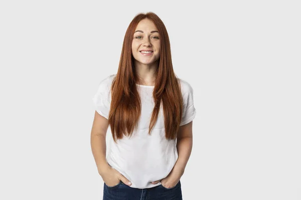 Portre fotoğraf genç duygusal Avrupa erkek gri arka plan üzerinde izole. Kızıl saçlı kız beyaz bir tişört. Kot pantolon ve o gülümsüyor ceplerinde elleri vardır.