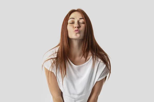 Giovane ragazza dai capelli rossi isolata su sfondo grigio in t-shirt bianca. Lei chiuse gli occhi e baciò — Foto Stock