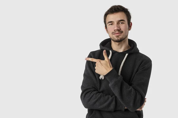 Tevreden Kaukasische jongeman wijzend op de lege ruimte en op zoek naar de camera. Geïsoleerd op een witte achtergrond. Advertentie concept. — Stockfoto