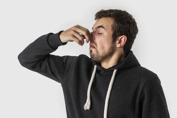 Αηδιασμένος Καυκάσιος νεαρός άνδρας κρατά τη μύτη του για να αποφύγετε την κακή μυρωδιά. Απομονωμένα σε λευκό φόντο. — Φωτογραφία Αρχείου