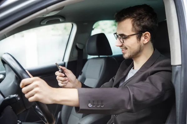 Il ragazzo e 'seduto alla sua macchina. Sta guardando le chiavi nella sua mano destra. La sua mano sinistra è sul volante . — Foto Stock