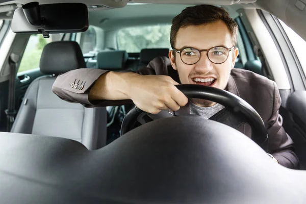 Fröhlicher junger Kerl blickt durch die Windschutzscheibe. er fährt Auto und hält Lenkrad mit beiden Händen. — Stockfoto