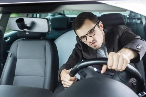 Woedend jonge bestuurder is op zoek via de windsheeld. Hij is zijn auto rijden en stuurwiel met beide handen te houden. — Stockfoto