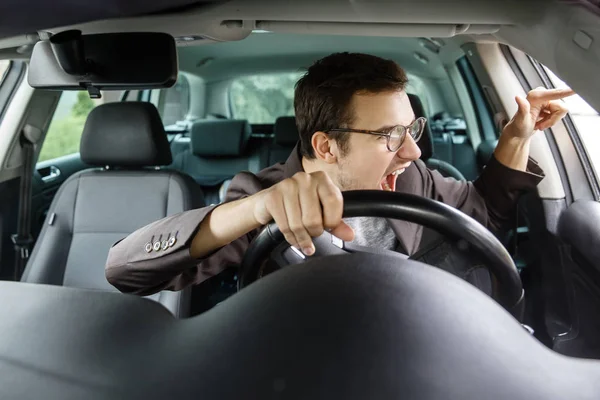 Furious young driver quarrels with other drivers. His right hand is on the steering wheel.