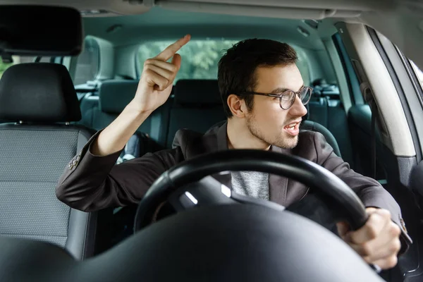 Boze jonge bestuurder ruzies met andere drivers. Zijn linkerhand is op het stuurwiel. — Stockfoto