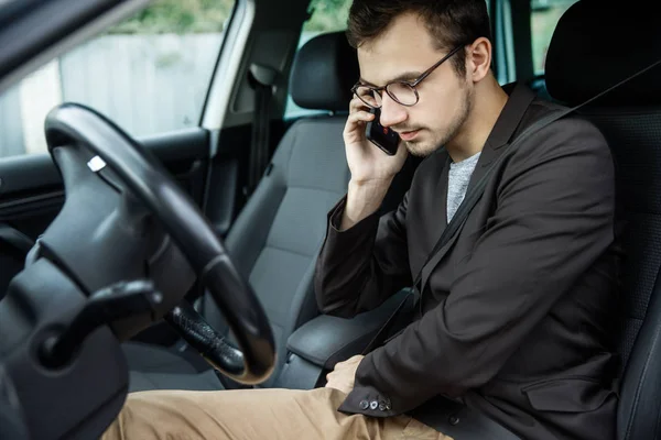 Fiatal srác klipsz-ra-a öv, miközben beszél a telefonon. Ő ül a kocsijában. Közúti biztonsági koncepció. — Stock Fotó