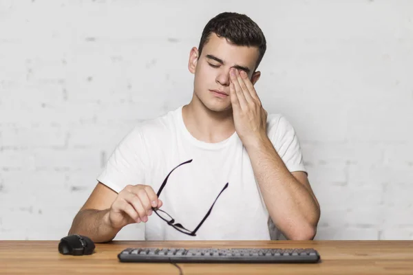 Genç adamın gözleri bilgisayar üzerinde çalıştıktan sonra zarar. Eliyle gözünü losyonları.