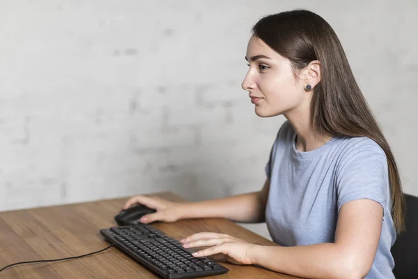 Девушка, работающая за компьютером. Она сидит за столом. . — стоковое фото
