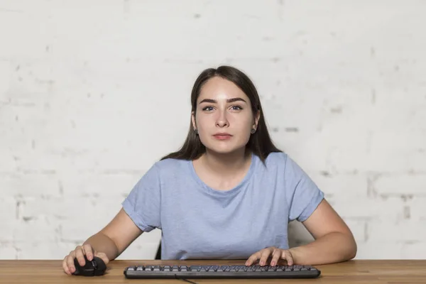 Девушка играет в компьютерную игру. Она смотрит прямо, рядом с ней клавиатура и мышка . — стоковое фото
