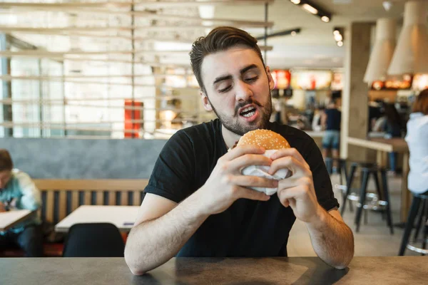 Lunch at the cafe. Greedy looks at the burger. — Stock Photo, Image