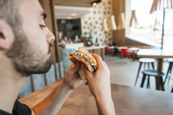 Close-up. Um homem está segurando um hambúrguer na mão no jantar — Fotografia de Stock