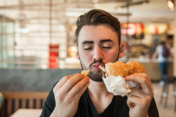 Lunch at the cafe. A man eats French fries and keeps a burger. — Stock Photo, Image