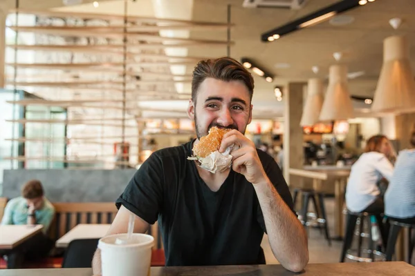 A man eats a burger at dinner in a cafe. — Stock Photo, Image