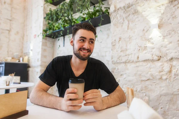 Bir adam bir kafede kahve elinde tutan bir masada oturuyor