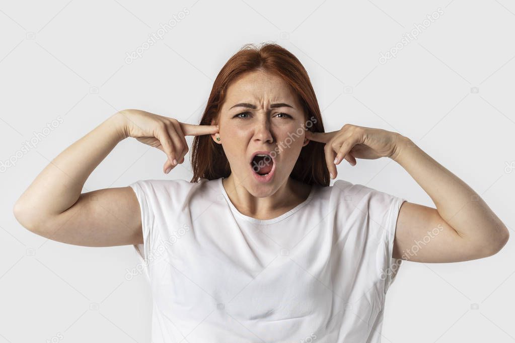 Young woman screams and plugging her ears with fingers and keeping eyes closed while having headache, can't stand terrible noise around from neighbours.