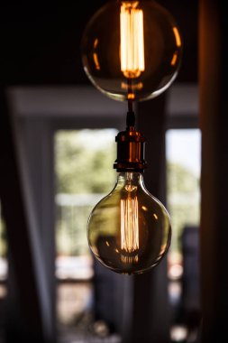 İki eski moda Edison kesimine tavandan asılı. Artalanları büyük bulanık penceresinde.