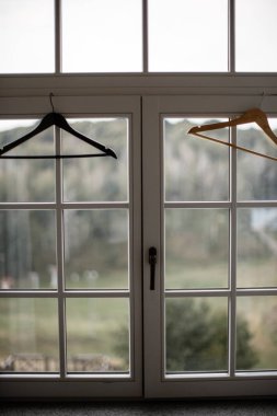 Üzerinde iki askıları olan büyük beyaz pencere. Arka planda bulanık arka bahçe. Gelinlik konsepti.